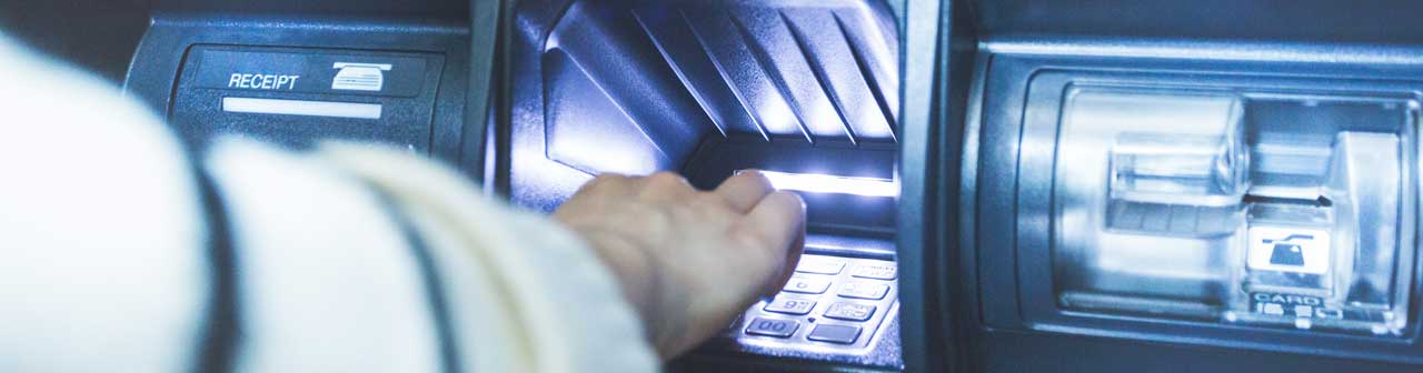 McCollisters A person’s hand reaches toward the keypad of a banking ATM, preparing to enter a PIN. The machine’s card slot and receipt dispenser are also visible, highlighting a typical moment in personal finance management.
