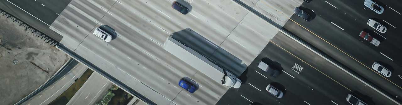 McCollisters Aerial view of multiple vehicles, including a large truck providing Final Mile delivery, driving on a multi-lane highway with cars traveling in both directions. The scene shows light to moderate traffic.