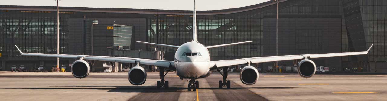 McCollisters A large passenger airplane is parked on the runway in front of a modern airport terminal building with glass windows.