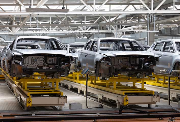 McCollisters Several unfinished car bodies are lined up on a car manufacturing assembly line inside a factory with bright overhead lighting and exposed beams, ready for OEMs to inspect before continuing to auto transport.