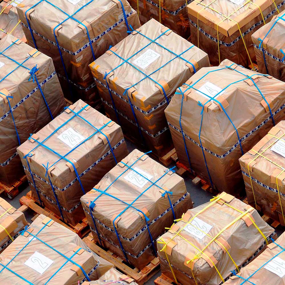 McCollisters Stacks of large, rectangular packages wrapped in brown paper and plastic, secured with colorful straps, are placed on wooden pallets for organized White Glove or Final Mile delivery service.