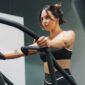 McCollisters A woman in athletic wear exercises on an elliptical machine in a gym, holding the handles and looking focused, surrounded by well-designed fitness spaces.