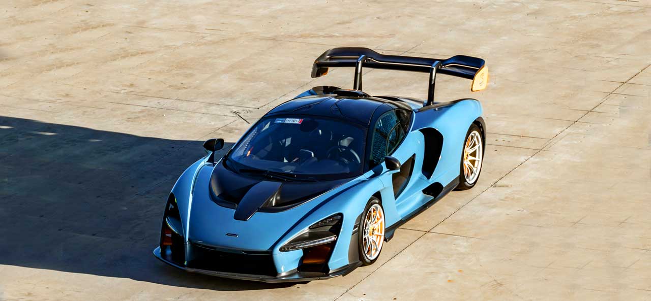 McCollisters A blue McLaren Senna sports car with a large rear wing is parked on a sunlit concrete surface, viewed from above—an ideal candidate for car shipping that emphasizes flexibility in auto transport solutions.